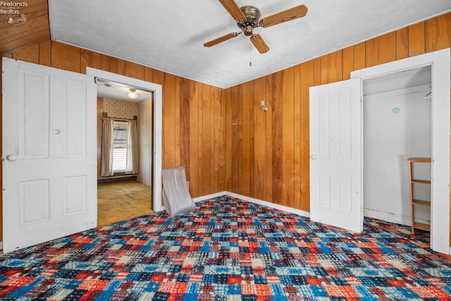 unfurnished bedroom with wood walls, a closet, ceiling fan, vaulted ceiling, and carpet