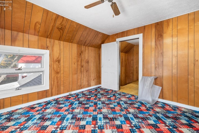 unfurnished room featuring wood walls, ceiling fan, a textured ceiling, and vaulted ceiling