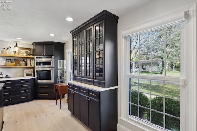 25 Edison, Milan, OH 44846 - kitchen featuring stainless steel double oven, light wood-style floors, dark cabinets, light countertops, and glass insert cabinets