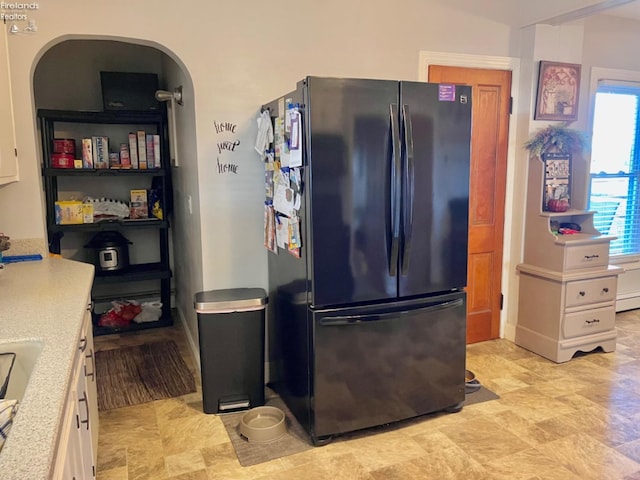 kitchen with baseboard heating, white cabinets, and black fridge