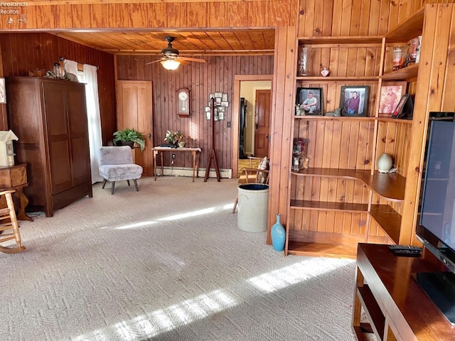 interior space featuring wood ceiling, wooden walls, carpet, a baseboard radiator, and ceiling fan