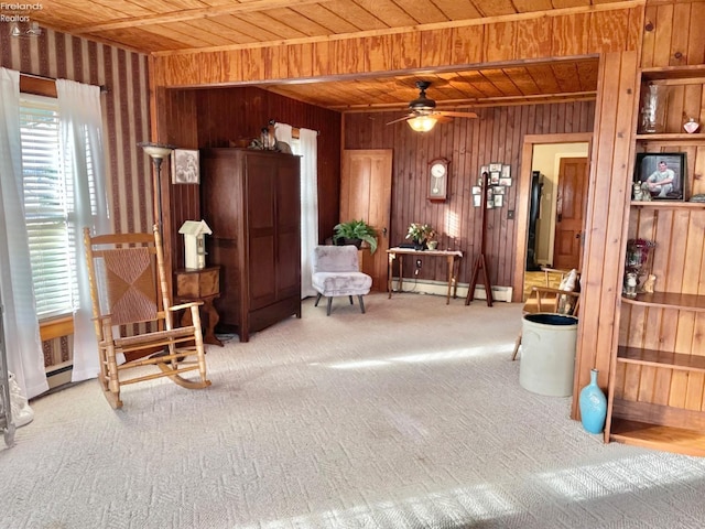 sitting room with wood walls, carpet flooring, a baseboard heating unit, wood ceiling, and ceiling fan