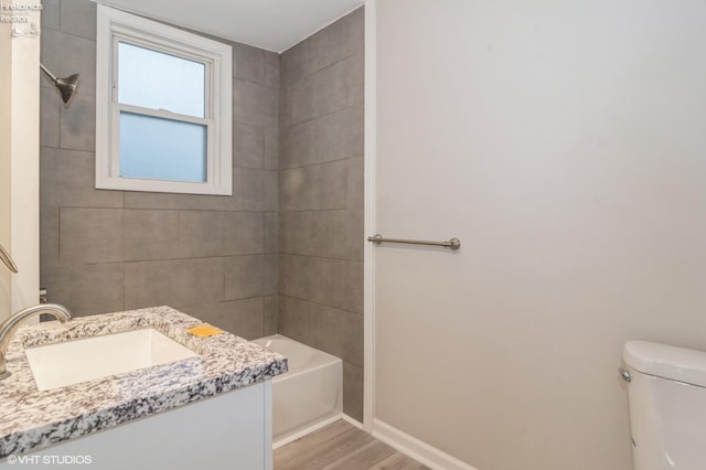 full bathroom featuring vanity, hardwood / wood-style floors, tiled shower / bath combo, and toilet