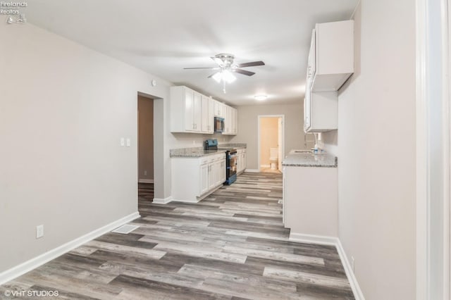 kitchen featuring black gas range, light hardwood / wood-style flooring, white cabinets, light stone counters, and ceiling fan