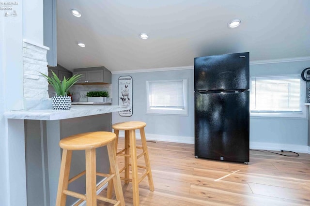 kitchen featuring black fridge, crown molding, a kitchen bar, gray cabinets, and light hardwood / wood-style flooring