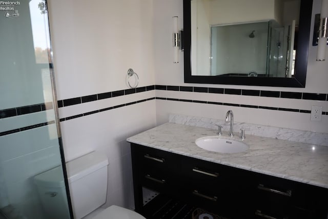 bathroom featuring toilet, vanity, walk in shower, and tile walls