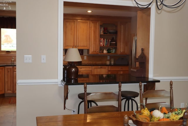 kitchen featuring dark stone countertops, light tile patterned floors, stainless steel fridge, and kitchen peninsula