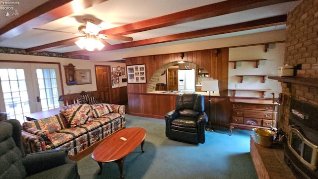 living room with french doors, carpet floors, wood walls, ceiling fan, and beam ceiling