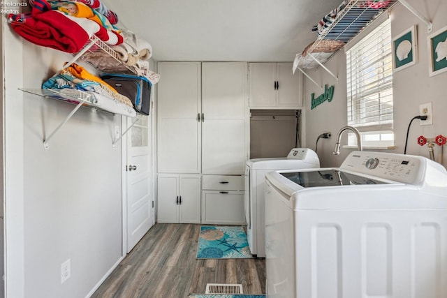 clothes washing area featuring hardwood / wood-style floors, cabinets, and washing machine and clothes dryer