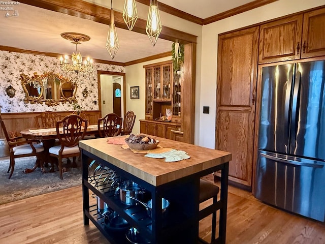 kitchen with crown molding, hanging light fixtures, stainless steel refrigerator, and light hardwood / wood-style flooring