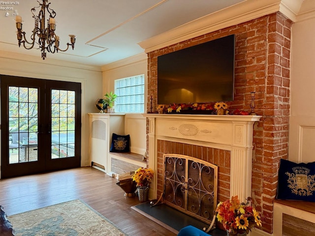 interior space featuring hardwood / wood-style floors, french doors, ornamental molding, a fireplace, and a chandelier