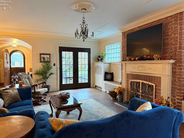 living room featuring a healthy amount of sunlight, wood-type flooring, ornamental molding, and a brick fireplace