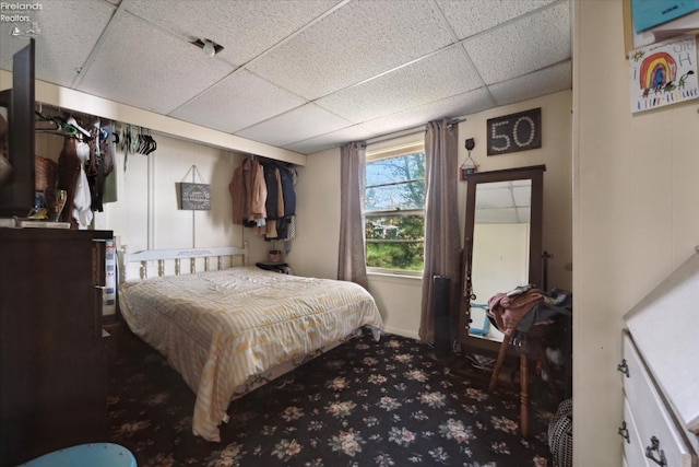 bedroom featuring dark colored carpet and a drop ceiling