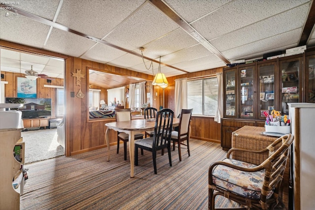 carpeted dining area featuring wood walls and a drop ceiling