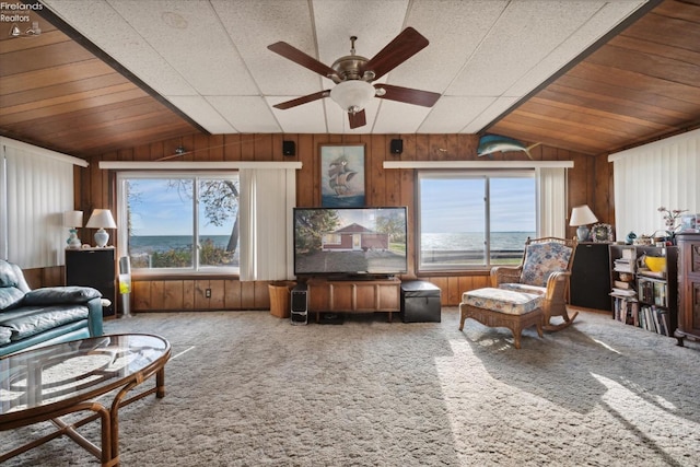 carpeted living room featuring ceiling fan, wooden walls, and lofted ceiling