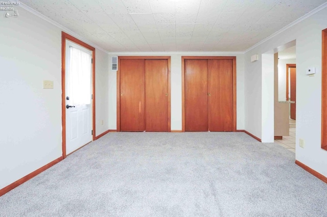 unfurnished bedroom featuring crown molding, light carpet, and two closets