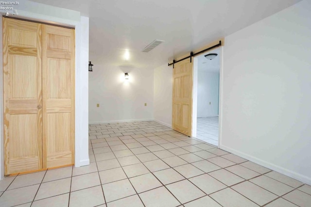 empty room with a barn door and light tile patterned floors