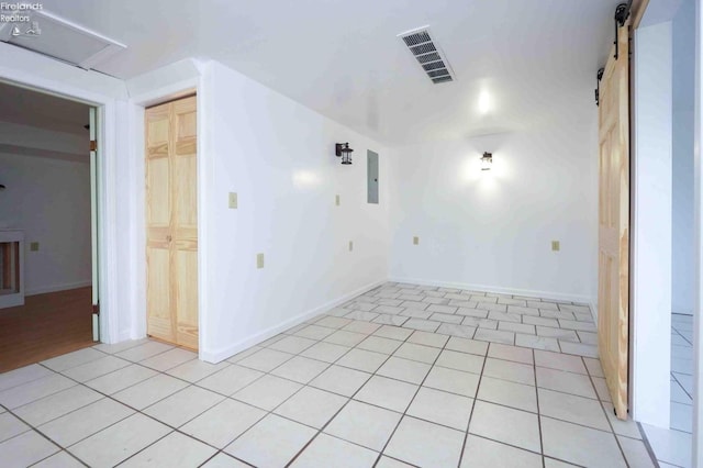 empty room with a barn door, light tile patterned floors, and electric panel