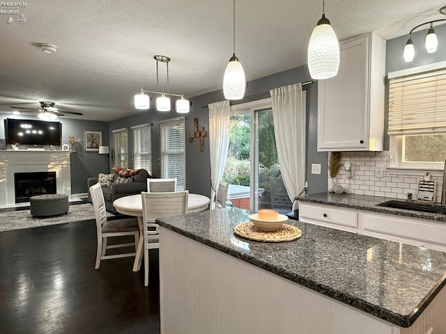 kitchen featuring tasteful backsplash, dark hardwood / wood-style floors, pendant lighting, white cabinets, and dark stone countertops