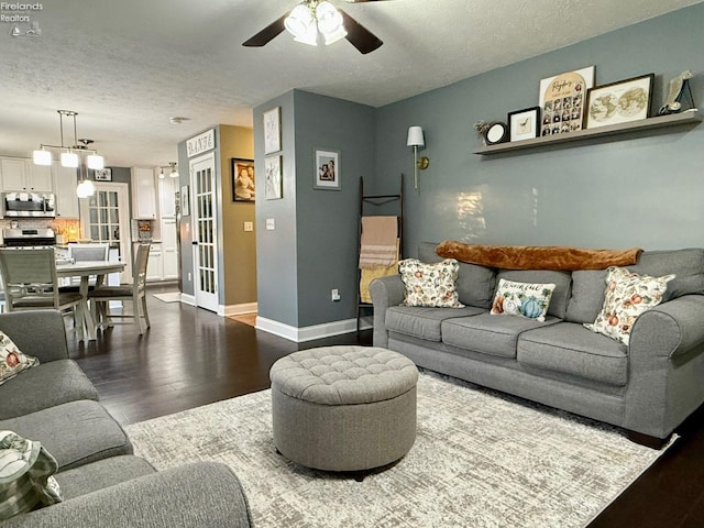 living room with ceiling fan with notable chandelier, dark wood-type flooring, and a textured ceiling