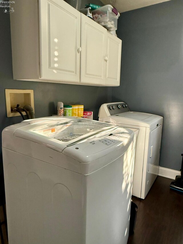 laundry area with dark hardwood / wood-style flooring, washing machine and dryer, and cabinets