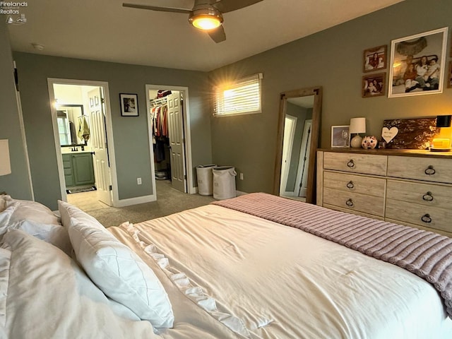 bedroom with a closet, a walk in closet, ensuite bath, light colored carpet, and ceiling fan