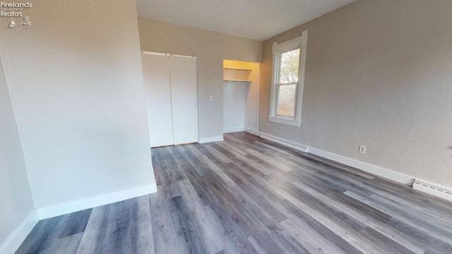 unfurnished room with dark hardwood / wood-style flooring and a baseboard heating unit