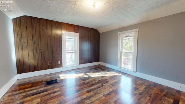 unfurnished room featuring wooden walls, a textured ceiling, dark hardwood / wood-style floors, and lofted ceiling