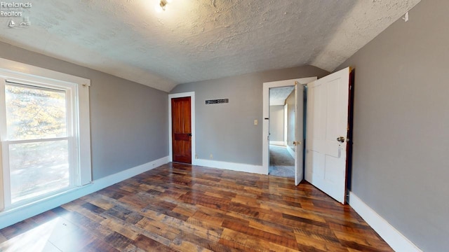 unfurnished bedroom with dark hardwood / wood-style flooring, a textured ceiling, and vaulted ceiling