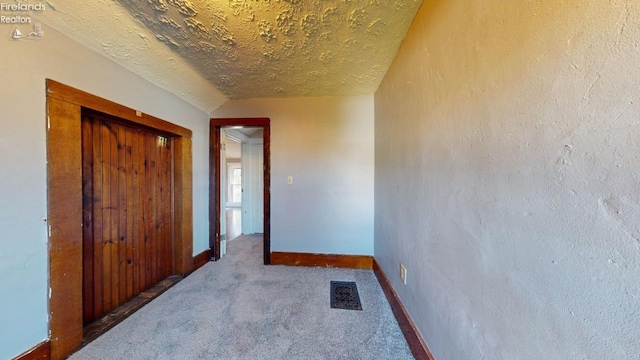 corridor with carpet, a textured ceiling, and vaulted ceiling