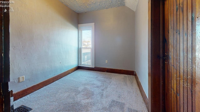 carpeted spare room with a textured ceiling and lofted ceiling
