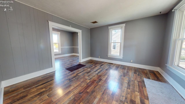 unfurnished room with dark hardwood / wood-style floors, plenty of natural light, and wood walls