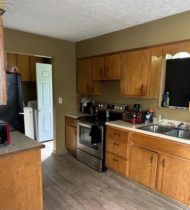 kitchen featuring sink, washing machine and dryer, light hardwood / wood-style flooring, black refrigerator, and stainless steel range with electric cooktop