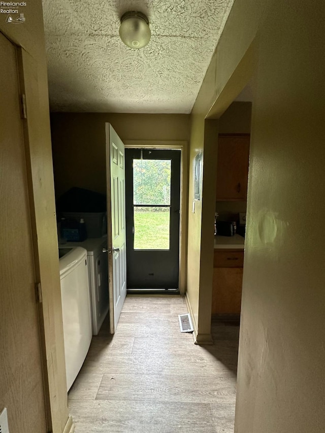 doorway to outside with independent washer and dryer, light wood-type flooring, and a textured ceiling