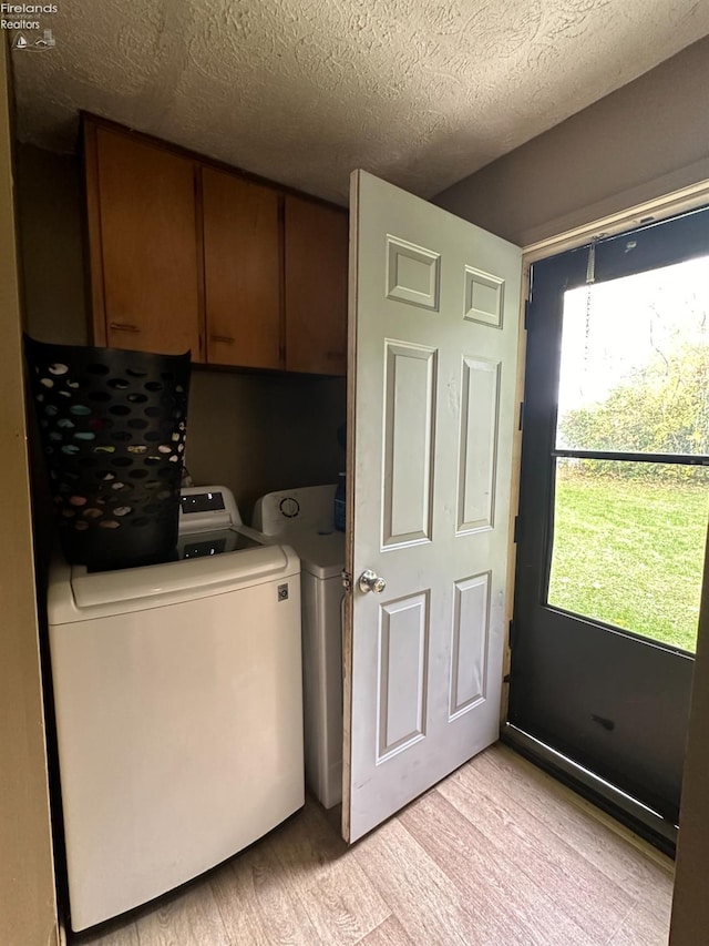 washroom featuring cabinets, light hardwood / wood-style floors, washing machine and dryer, and a textured ceiling