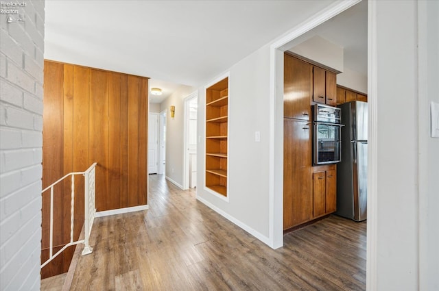 kitchen featuring wood-type flooring, black oven, built in shelves, and stainless steel refrigerator