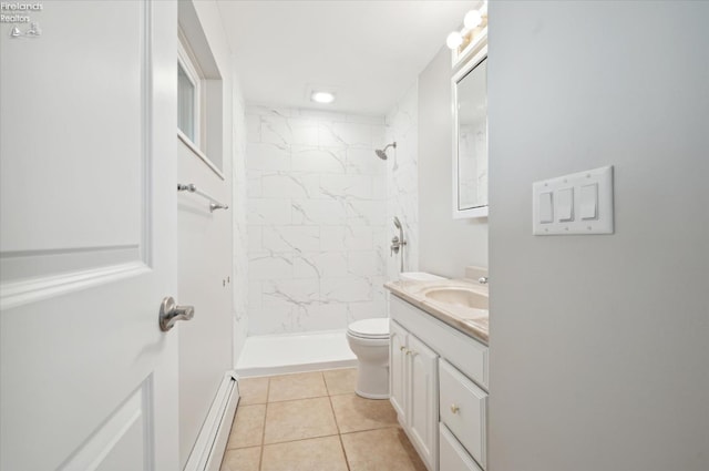 bathroom with a tile shower, baseboard heating, tile patterned floors, toilet, and vanity