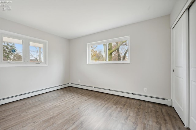 unfurnished bedroom with hardwood / wood-style floors, a baseboard radiator, and a closet