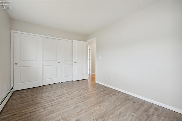 unfurnished bedroom featuring light hardwood / wood-style flooring, a closet, and a baseboard heating unit