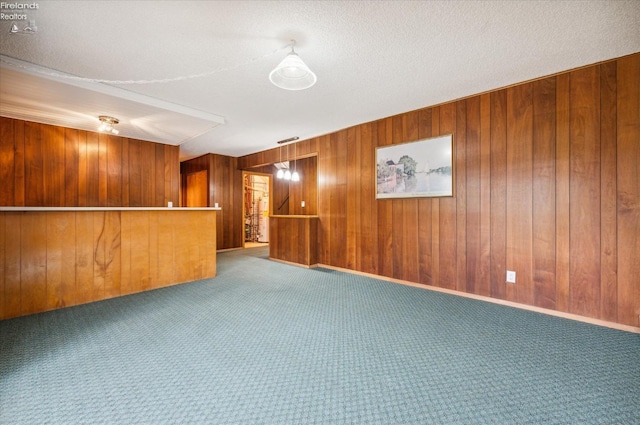 carpeted spare room with wood walls and a textured ceiling