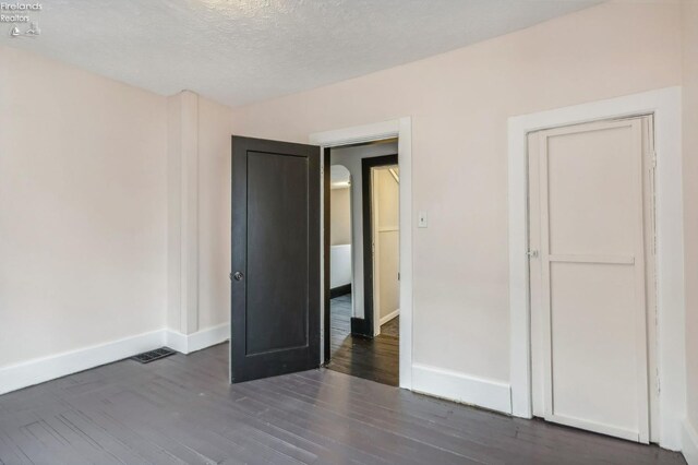 unfurnished bedroom with a textured ceiling and dark hardwood / wood-style floors