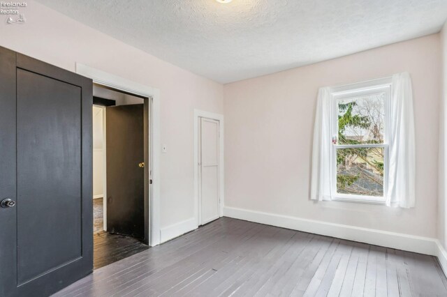 unfurnished bedroom with a textured ceiling, a closet, and dark hardwood / wood-style floors