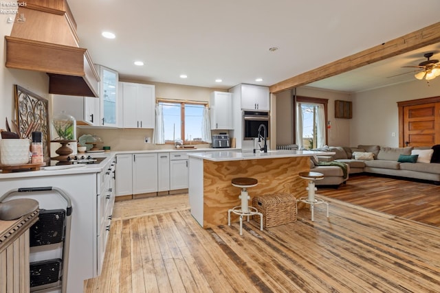 kitchen with a breakfast bar, ceiling fan, white cabinets, light hardwood / wood-style floors, and a kitchen island