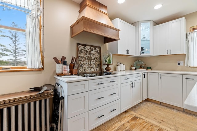 kitchen featuring radiator, black electric stovetop, light hardwood / wood-style flooring, custom range hood, and white cabinetry