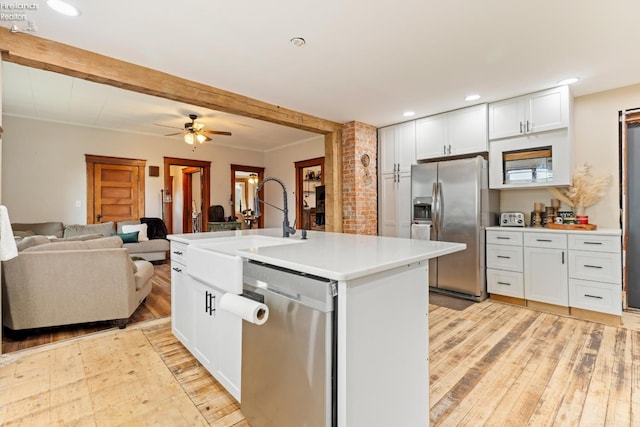 kitchen with white cabinets, a center island with sink, ceiling fan, light wood-type flooring, and appliances with stainless steel finishes