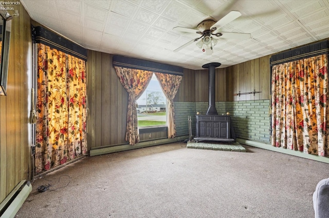 interior space with baseboard heating, a wood stove, ceiling fan, and carpet