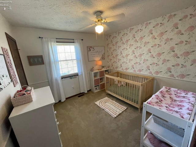 bedroom featuring a textured ceiling, ceiling fan, a crib, and carpet floors