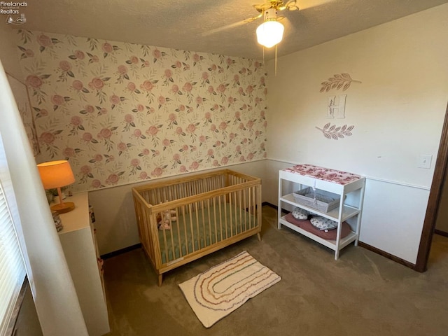 bedroom with dark colored carpet, a textured ceiling, a nursery area, and ceiling fan