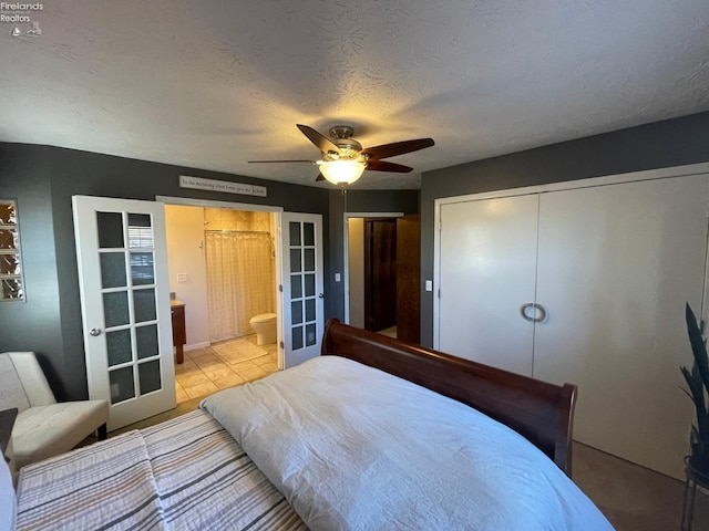 tiled bedroom with french doors, ensuite bathroom, ceiling fan, a textured ceiling, and a closet