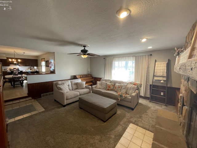 living room featuring a textured ceiling, a stone fireplace, and ceiling fan